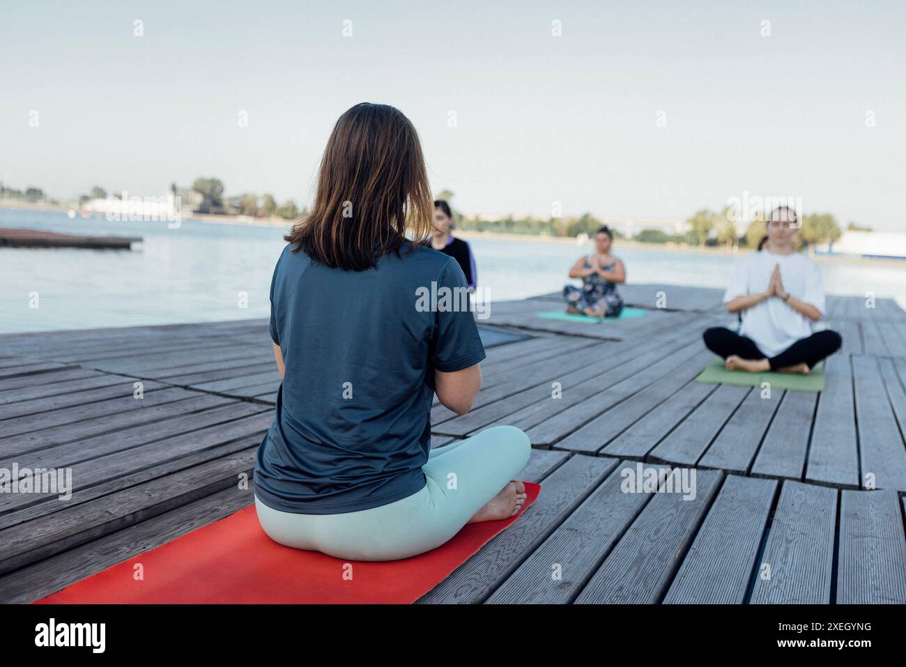 Yoga-Kurs im Freien mit einem Lehrer in der Nähe des Flusses. Junge Frauen sitzen im Kreuz auf Matten Stockfoto