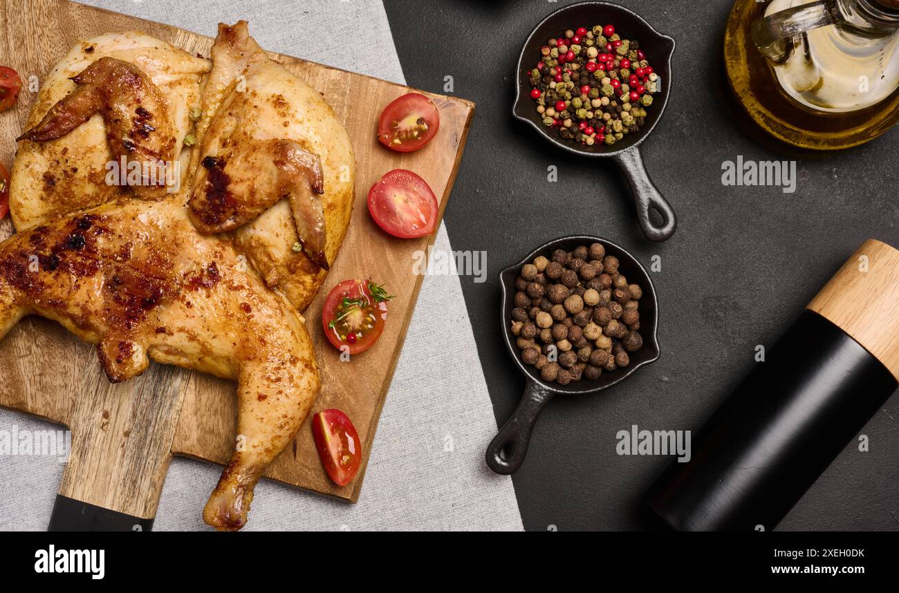 Ganze gebratene Hühnchen mit Gewürzen auf einem Holzbrett auf einem schwarzen Tisch Stockfoto