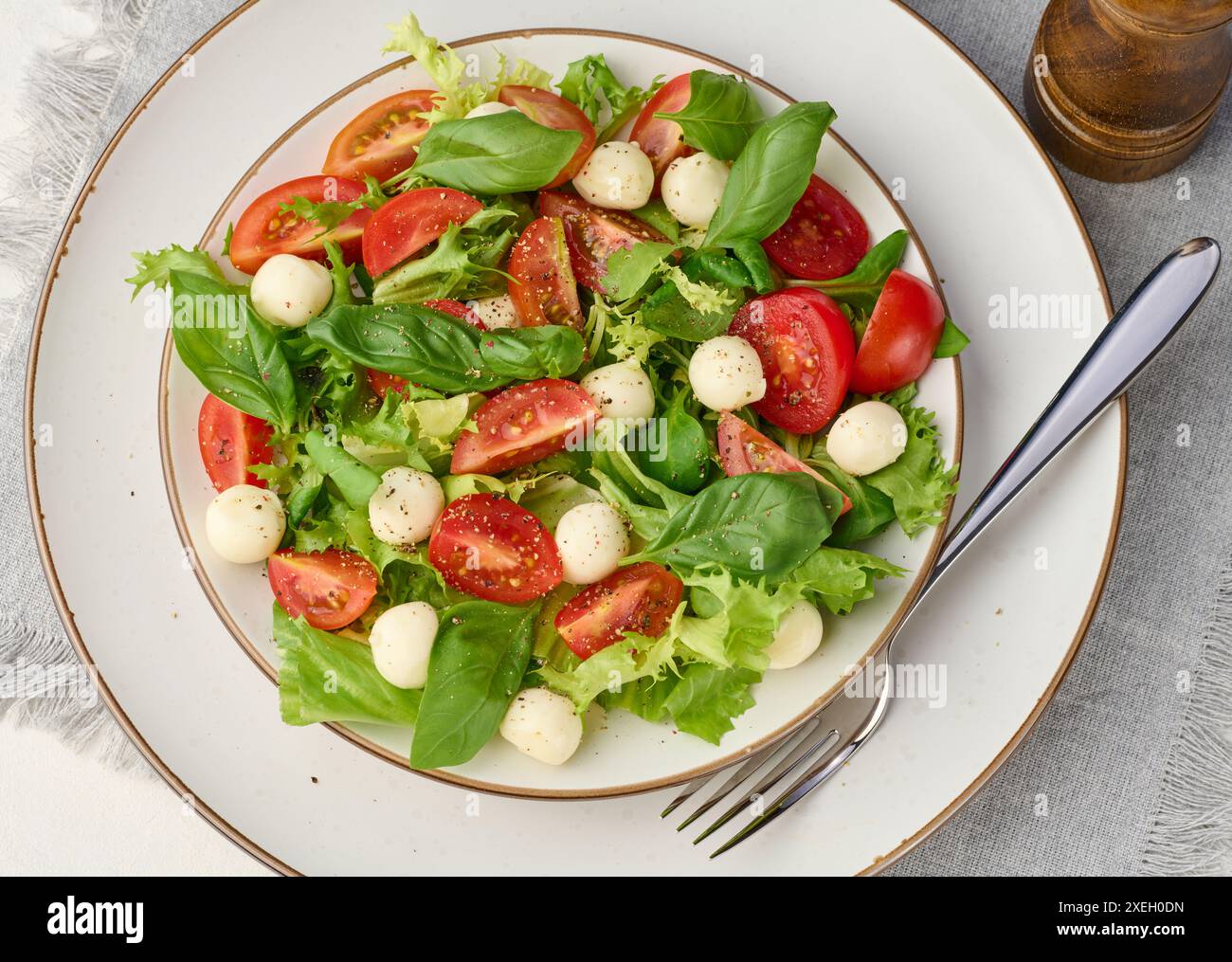 Salat mit Mozzarella, Kirschtomaten und grünem Salat auf einem weißen runden Teller auf dem Tisch Stockfoto