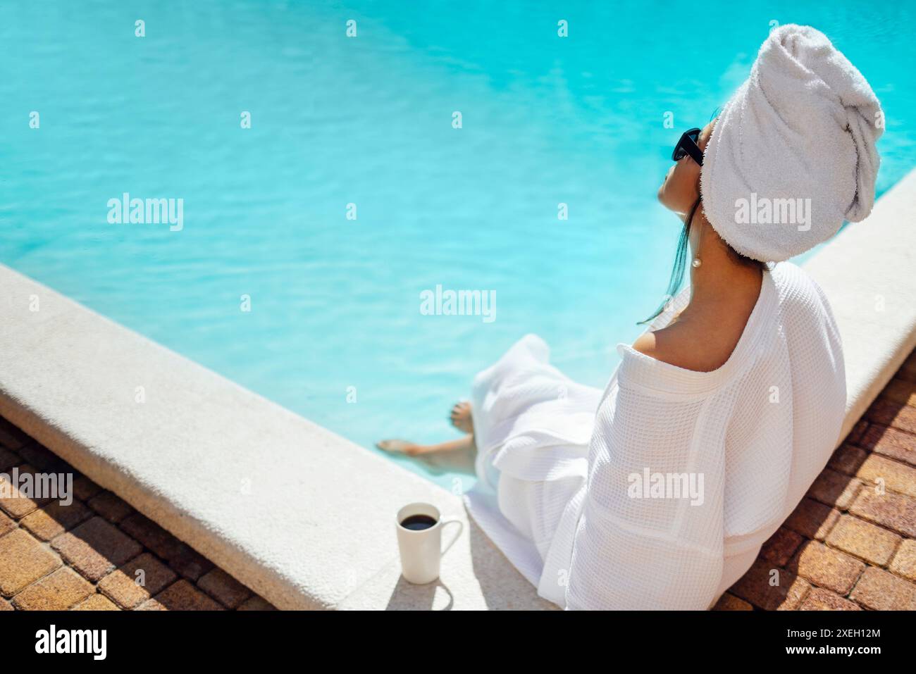 Die junge hübsche Frau in einem weißen Bademantel hält eine Tasse Kaffee. Stockfoto