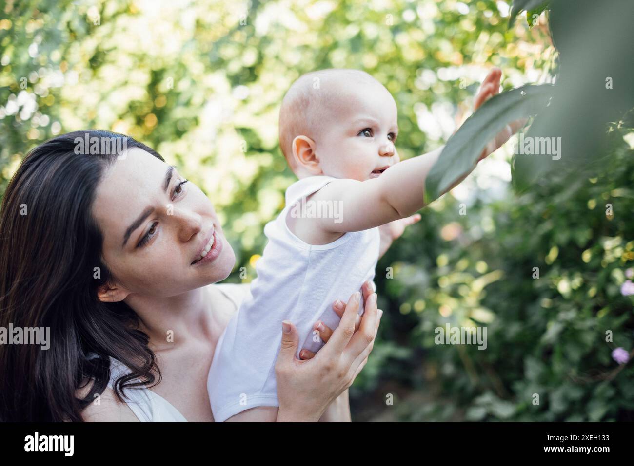 Nahaufnahme des weiblichen Porträts einer jungen charmanten Mutter hält ihr süßes Baby im Garten Stockfoto