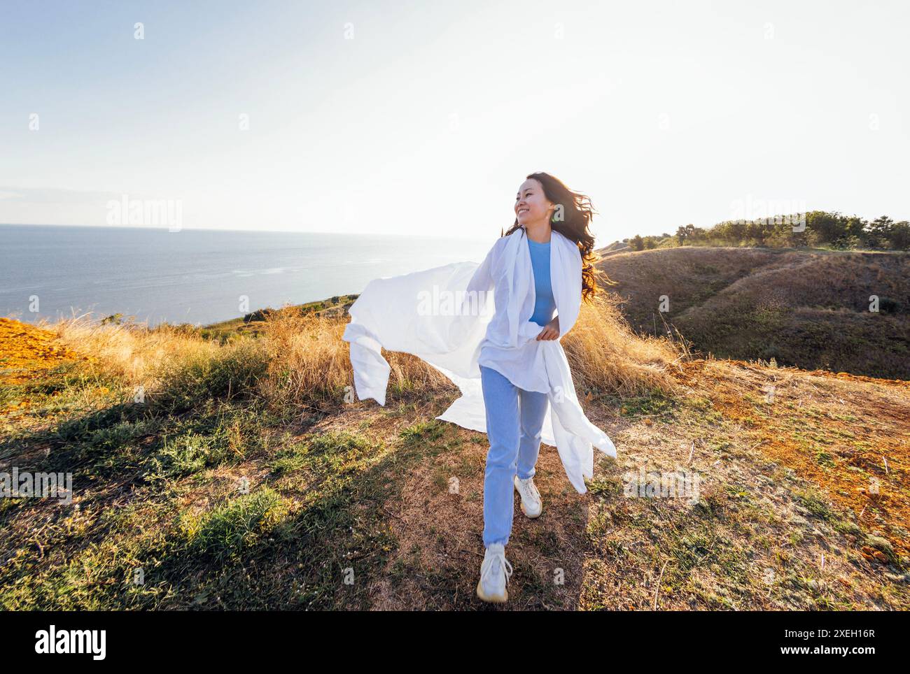 Eine süße asiatische Frau lacht und rennt mit einem weißen Laken im Freien. Ein charmantes koreanisches Mädchen genießt Natur und Freiheit. Ein Pret Stockfoto