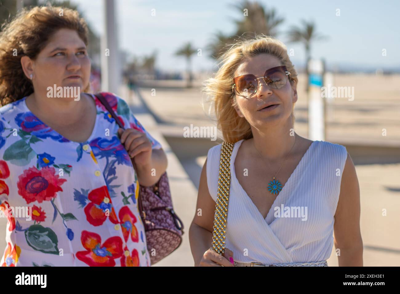 Dieses Bild zeigt zwei Frauen, die einen gemütlichen Spaziergang auf einer Strandpromenade machen. Beide Frauen sind stilvoll gekleidet, wobei eine Frau ein lebendiges f Stockfoto
