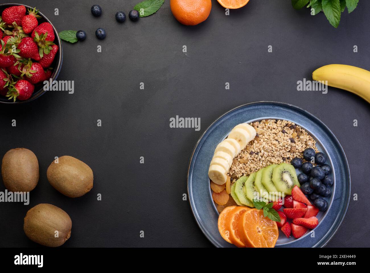 Müsli mit Erdbeeren, Kiwi, Banane und Heidelbeeren in einem runden Teller auf einem schwarzen Tisch. Gesundes und leckeres Essen Stockfoto
