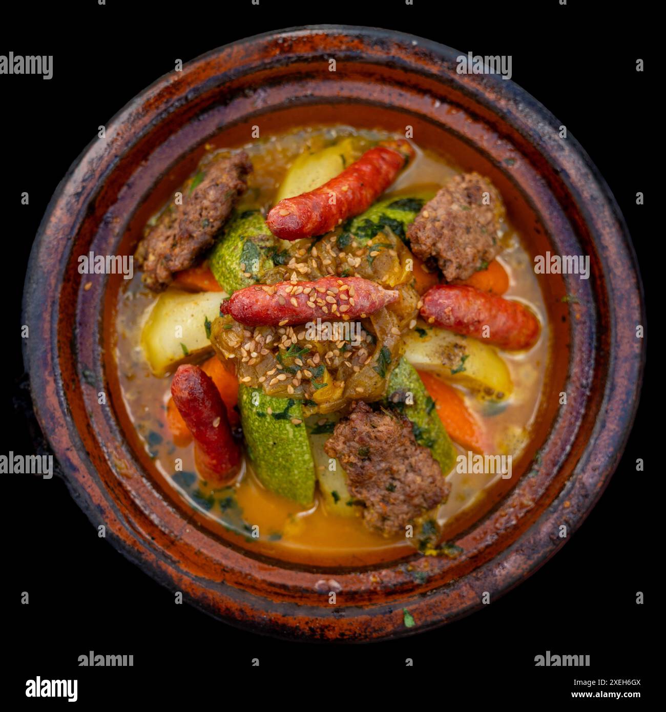 Blick von oben auf ein Tagine Royal Gericht mit Gemüse und verschiedenen Fleischsorten und orientalischen Gewürzen auf schwarzem Hintergrund Stockfoto