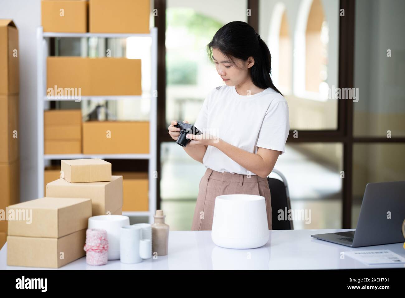 Junger asiatischer Unternehmer, der eine kompakte Digitalkamera verwendet, macht ein Foto des Produkts, um es in den Online-Shop der Website hochzuladen. Stockfoto