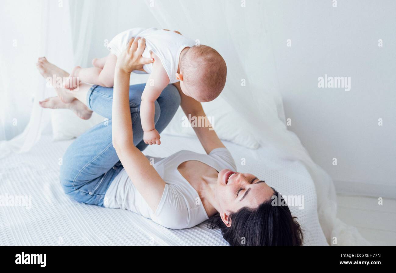Hübsches Kind in einem weißen Body mit seiner Mutter auf hellem Hintergrund. Mutterschaftskonzept. Stockfoto