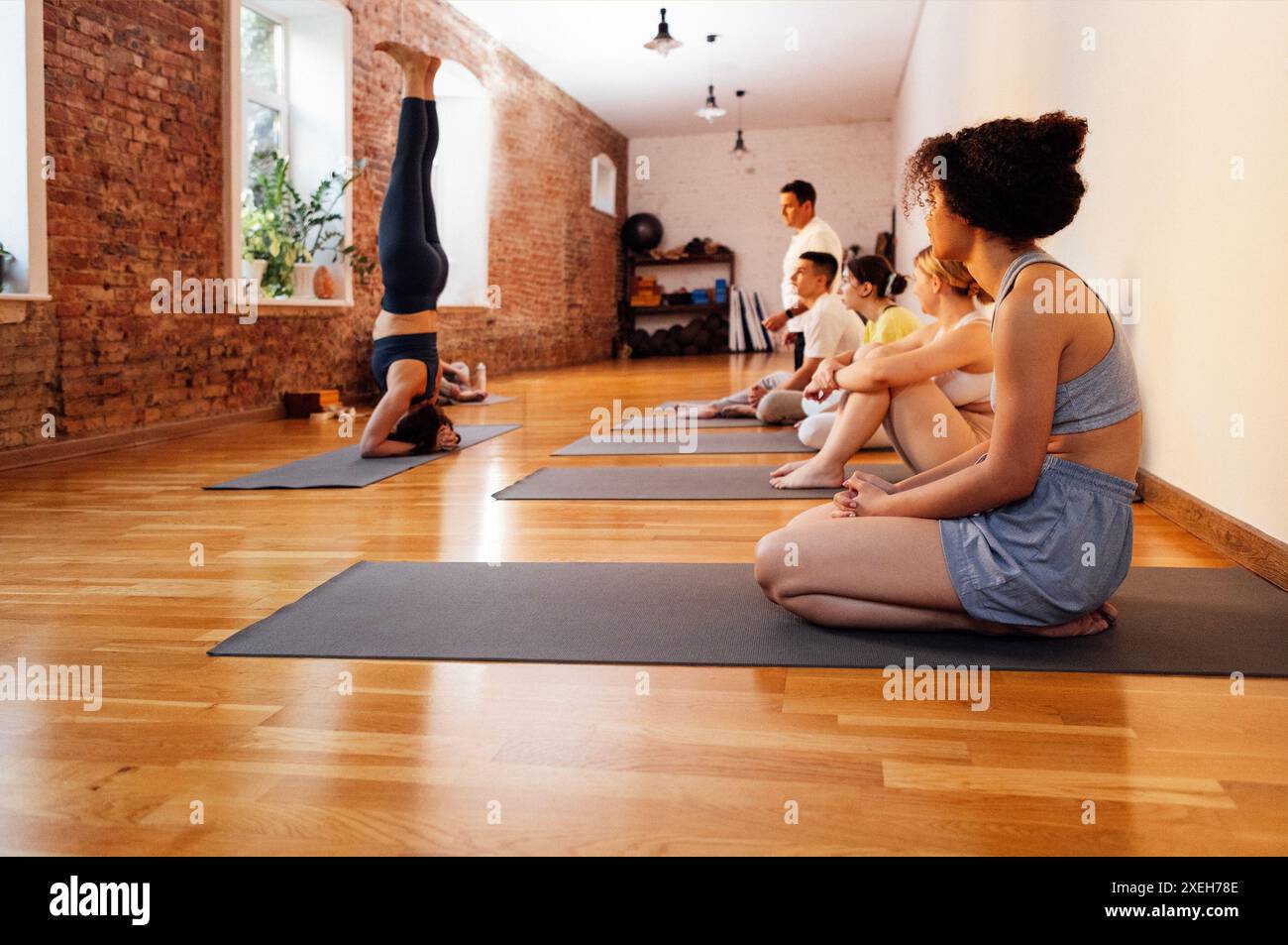 Der Coach zeigt den Schülern den Kopfstand. Eine Gruppe von Menschen unterschiedlichen Alters und Ethnien macht Yoga in einem Fitnessclub. Yo Stockfoto