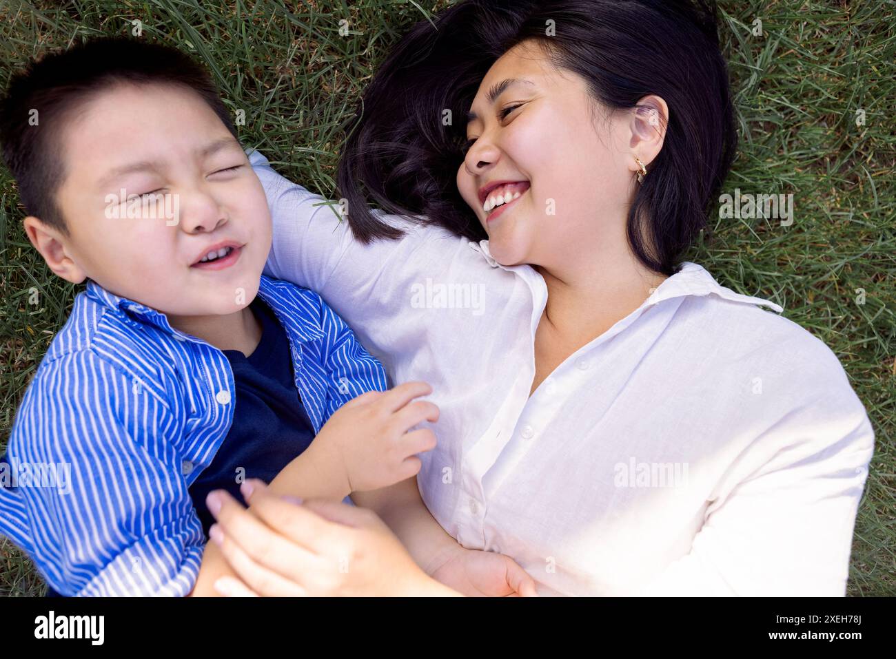Asiatische lachende Mutter und Sohn liegen auf einem grünen Rasen Stockfoto