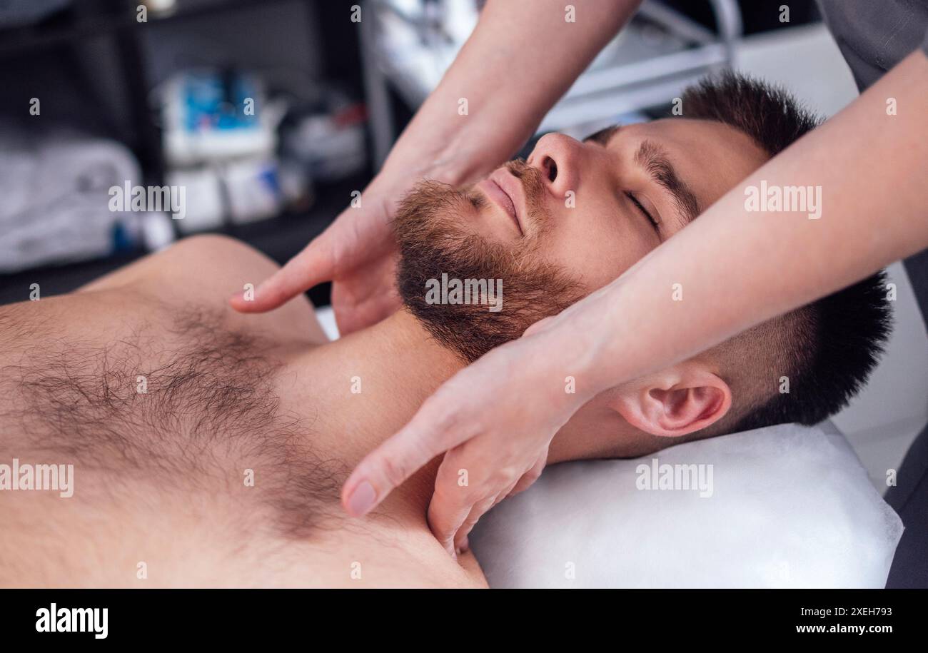 Nahporträt eines jungen attraktiven Mannes, der eine Gesichtsmassage bekommt Stockfoto