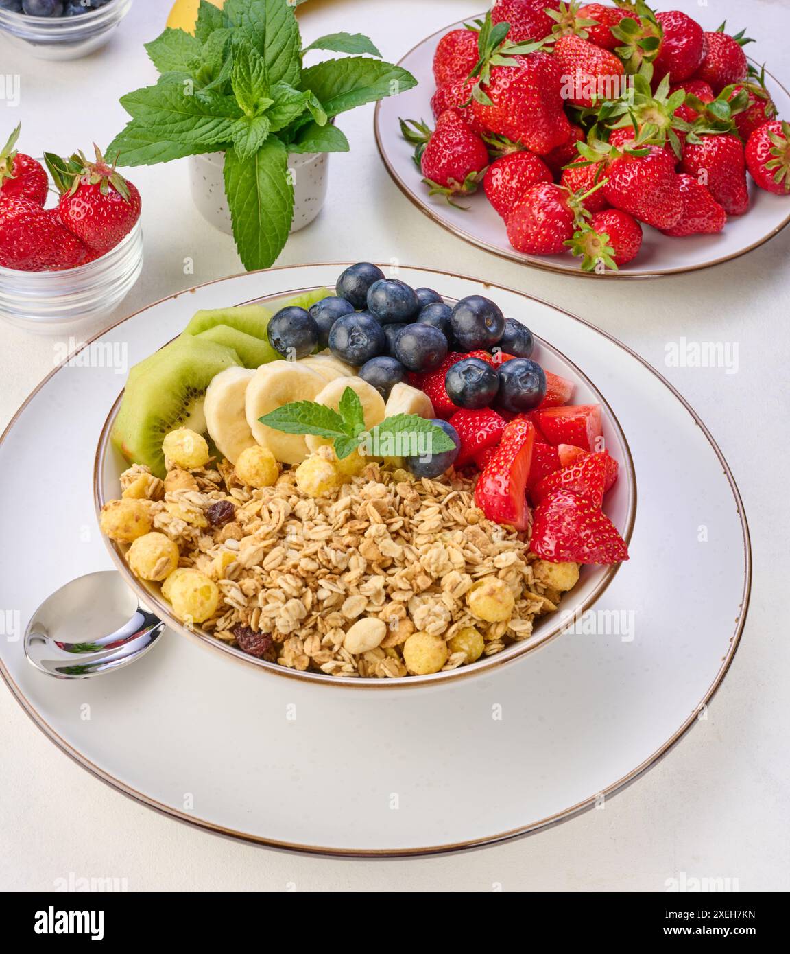 Müsli mit Erdbeeren, Kiwi, Banane und Heidelbeeren in einem runden Teller auf einem weißen Tisch. Stockfoto