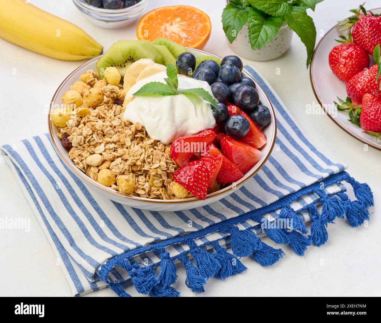 Müsli mit Erdbeeren, Kiwi, Banane und Heidelbeeren in einem runden Teller auf einem weißen Tisch. Stockfoto
