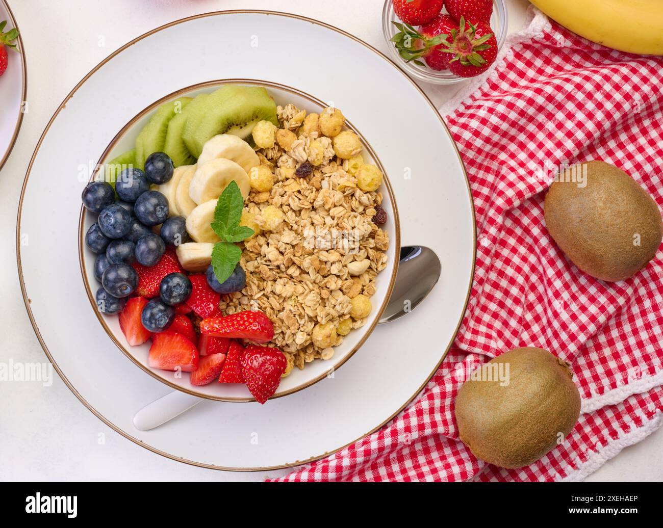 Müsli mit Erdbeeren, Kiwi, Banane und Heidelbeeren in einem runden Teller auf einem weißen Tisch. Stockfoto