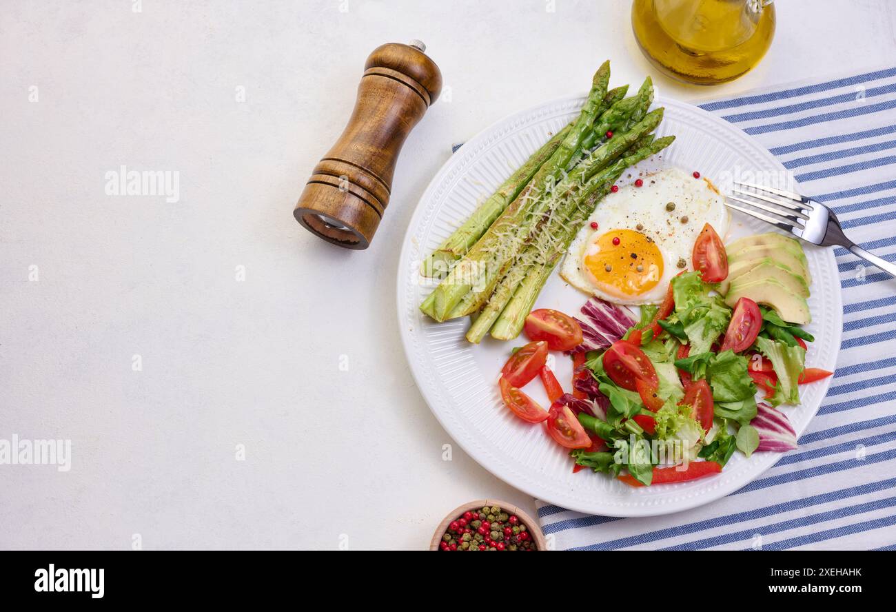 Runder Teller mit gekochtem Spargel, Spiegelei, Avocado und frischem Gemüsesalat auf dem Tisch, Blick von oben Stockfoto