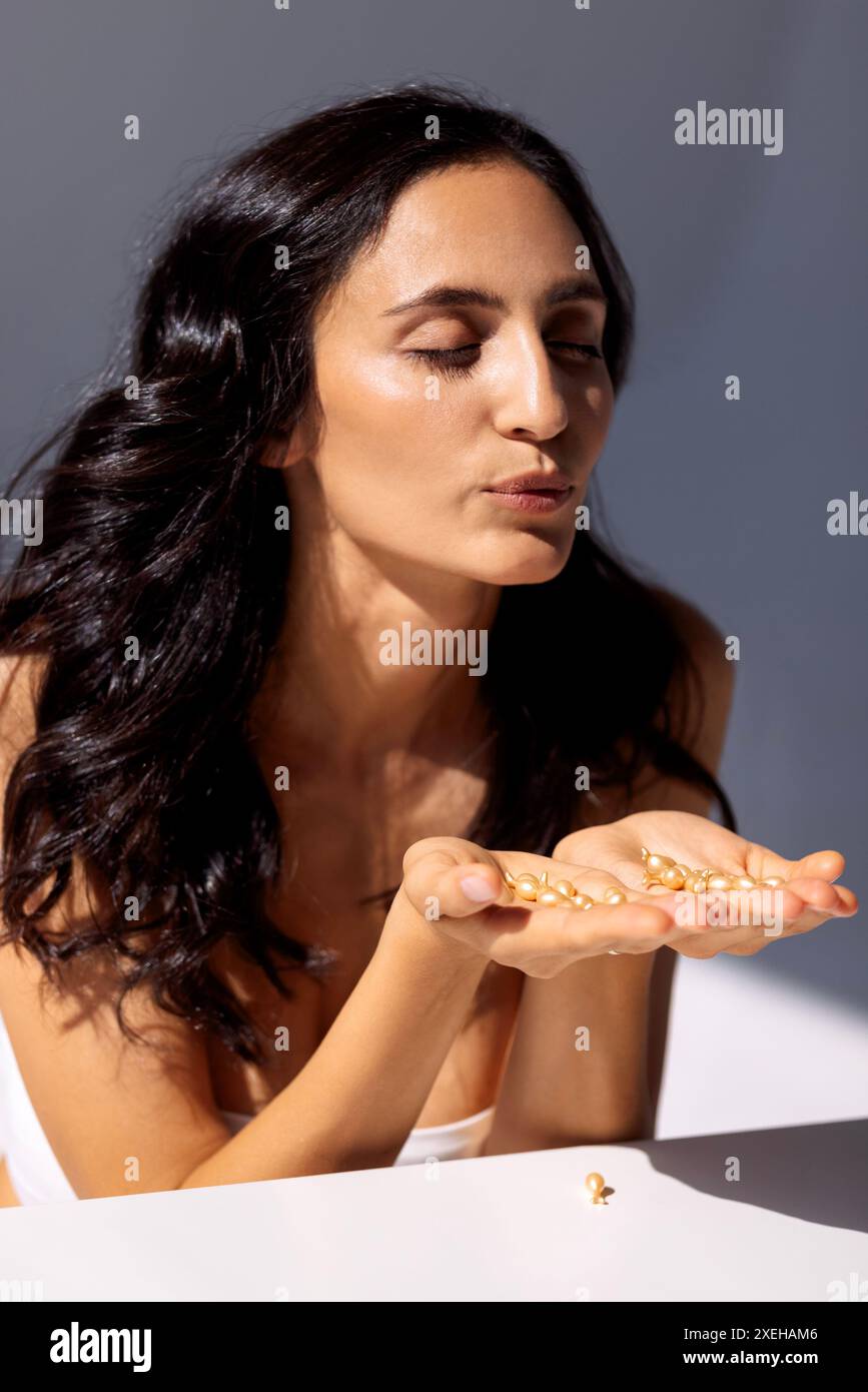 Junge Frau mit gesunder Haut hält Kapseln mit feuchtigkeitsspendendem Gesichtsserum mit Hyaluronsäure. Stockfoto