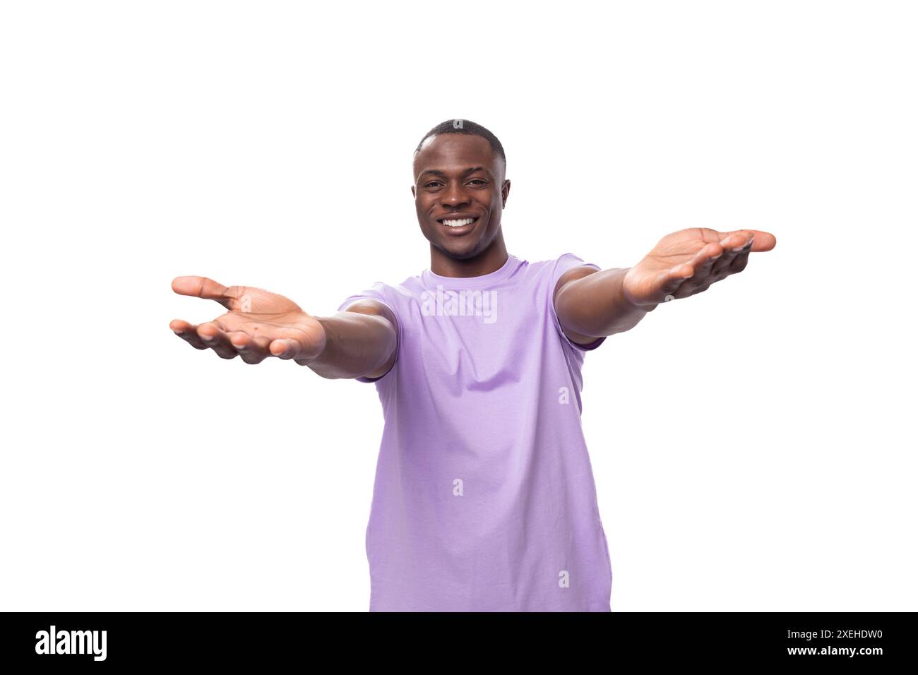 Junger freundlicher, unbeschwerter amerikanischer Mann, gekleidet in einem Flieder-T-Shirt auf weißem Hintergrund mit Kopierraum Stockfoto