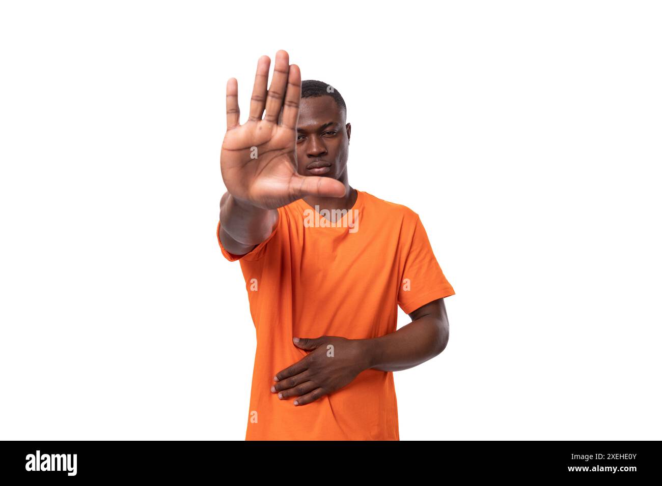 Ein junger seriöser Amerikaner mit einem kurzen Haarschnitt in einem orangen T-Shirt zeigt mit seiner Hand auf weißem Hintergrund Stockfoto