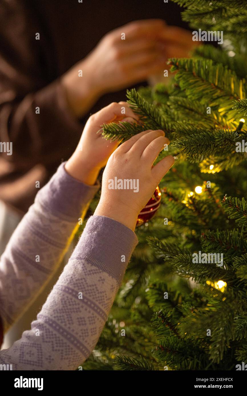 Kinderhände hängen weihnachtsschmuck in einen weihnachtsbaum Stockfoto