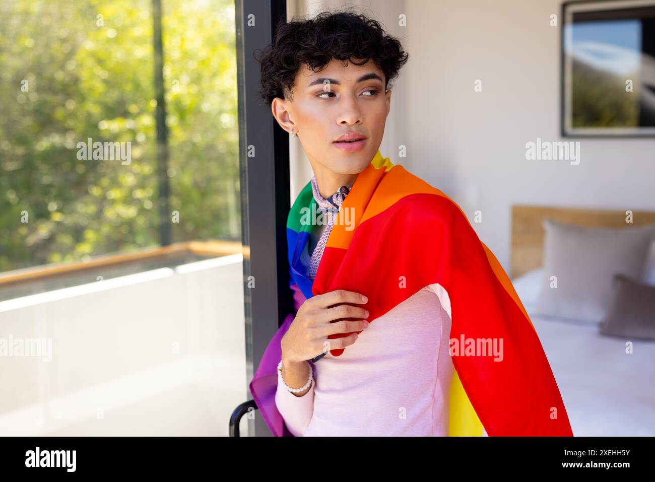 Die Regenbogenfahne trägt eine Transgender-Transgender-Frau, die zu Hause am Fenster steht Stockfoto