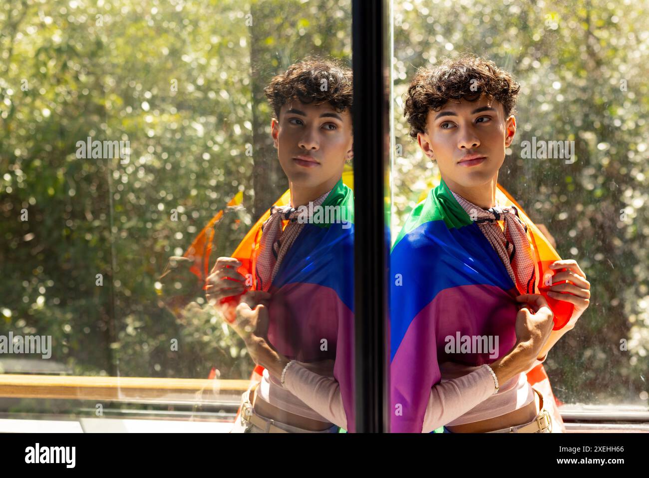 Mit Regenbogenfahne, Transgender-Frau, die am Fenster steht, mit Spiegelglas Stockfoto