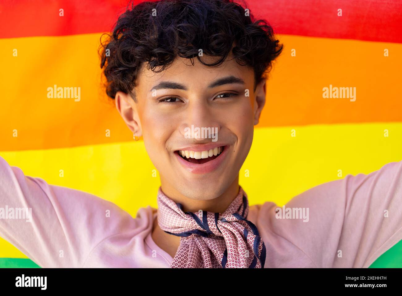 Ein lächelnder junger Mann, der die Regenbogenfahne hält, feiert den Stolz und die Identität der Transgender Stockfoto