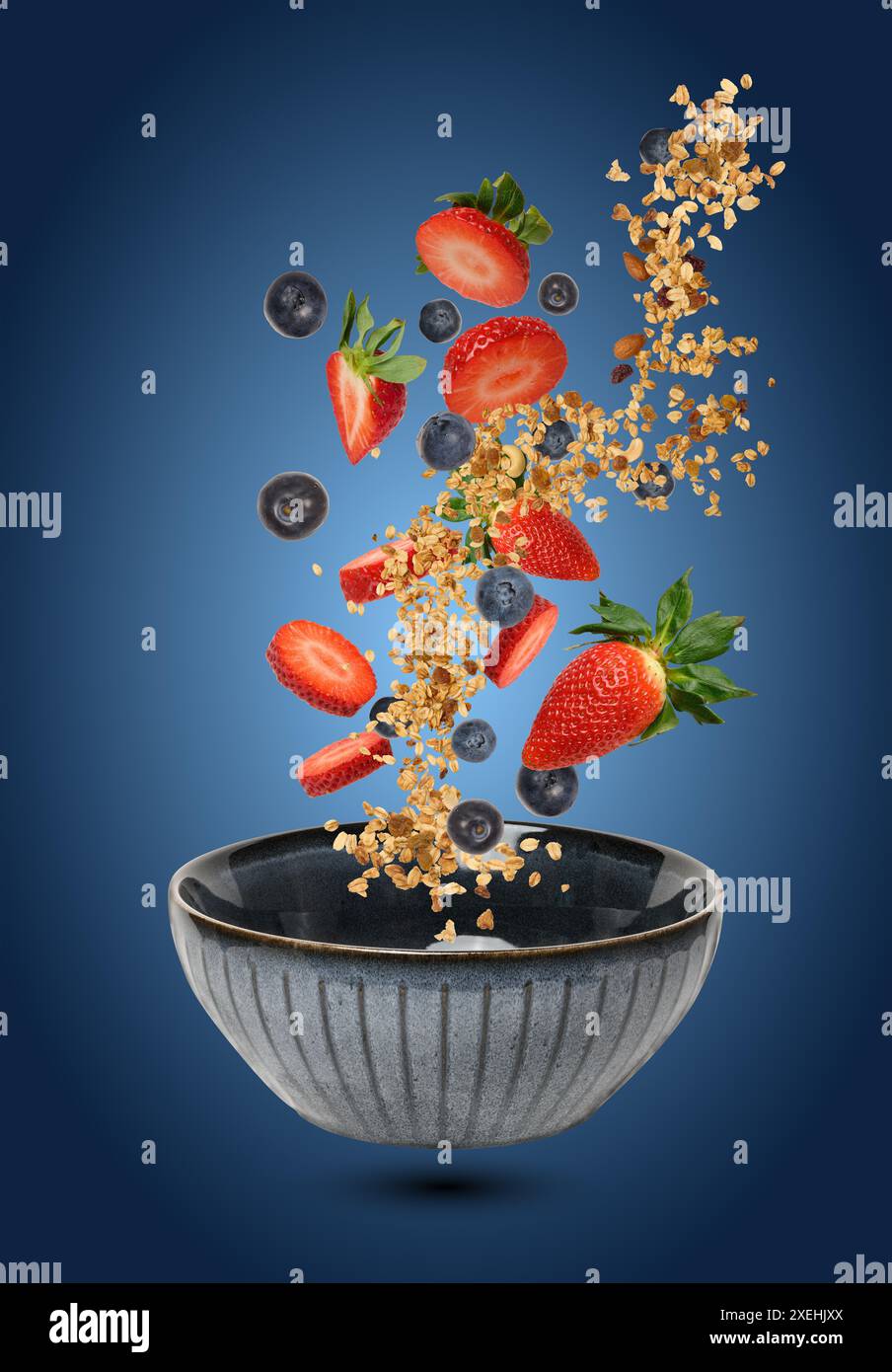 Eine Keramikschale, in der Erdbeeren, Heidelbeeren und Müsli in der Luft schweben und fallen, um ein dynamisches Gefühl zu erzeugen Stockfoto