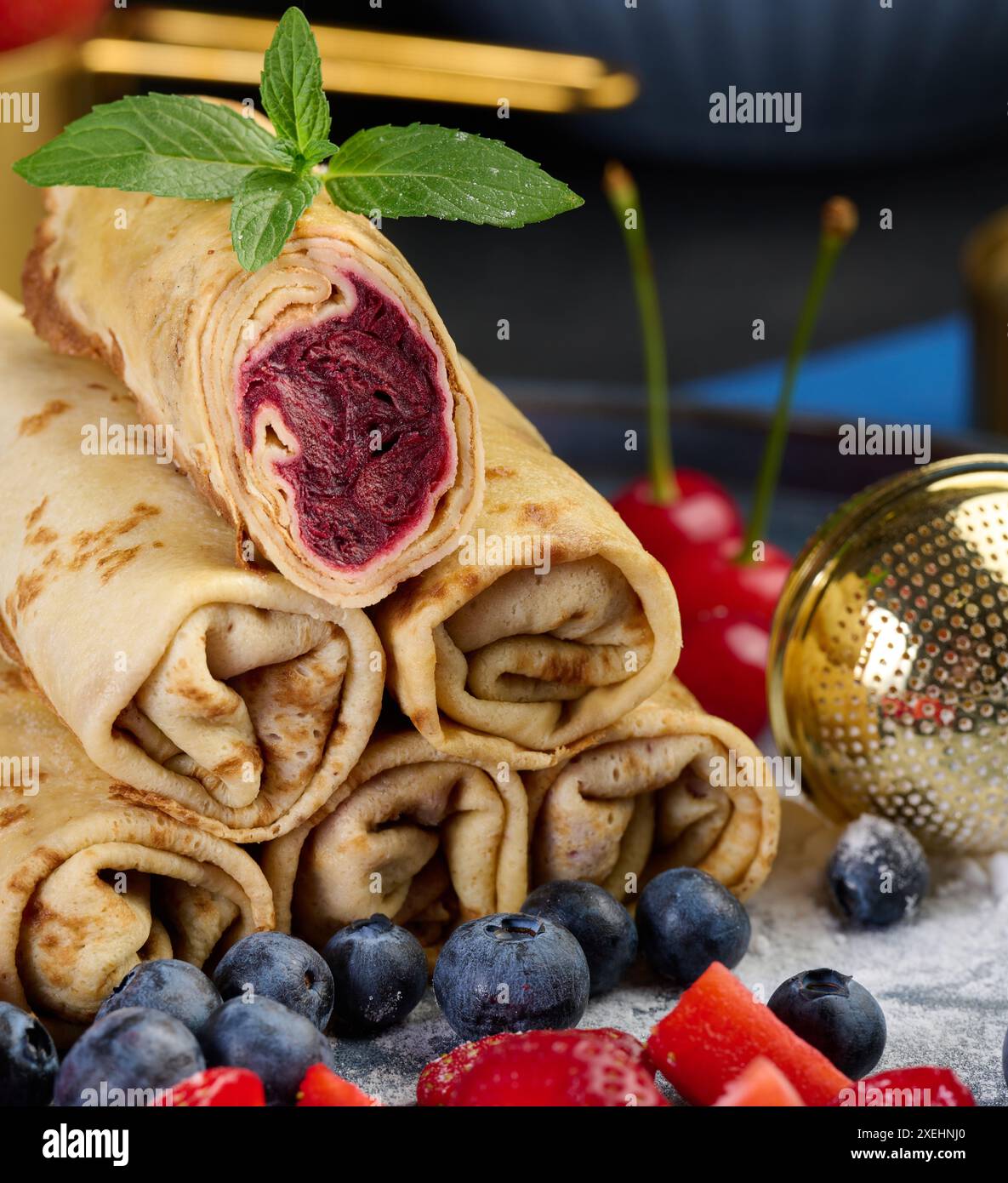 Crepes stapeln sich auf einem Stapel, von denen einer geschnitten und mit Beerenfüllung gefüllt ist. Der Teller ist auch mit Heidelbeeren und Stroh verziert Stockfoto