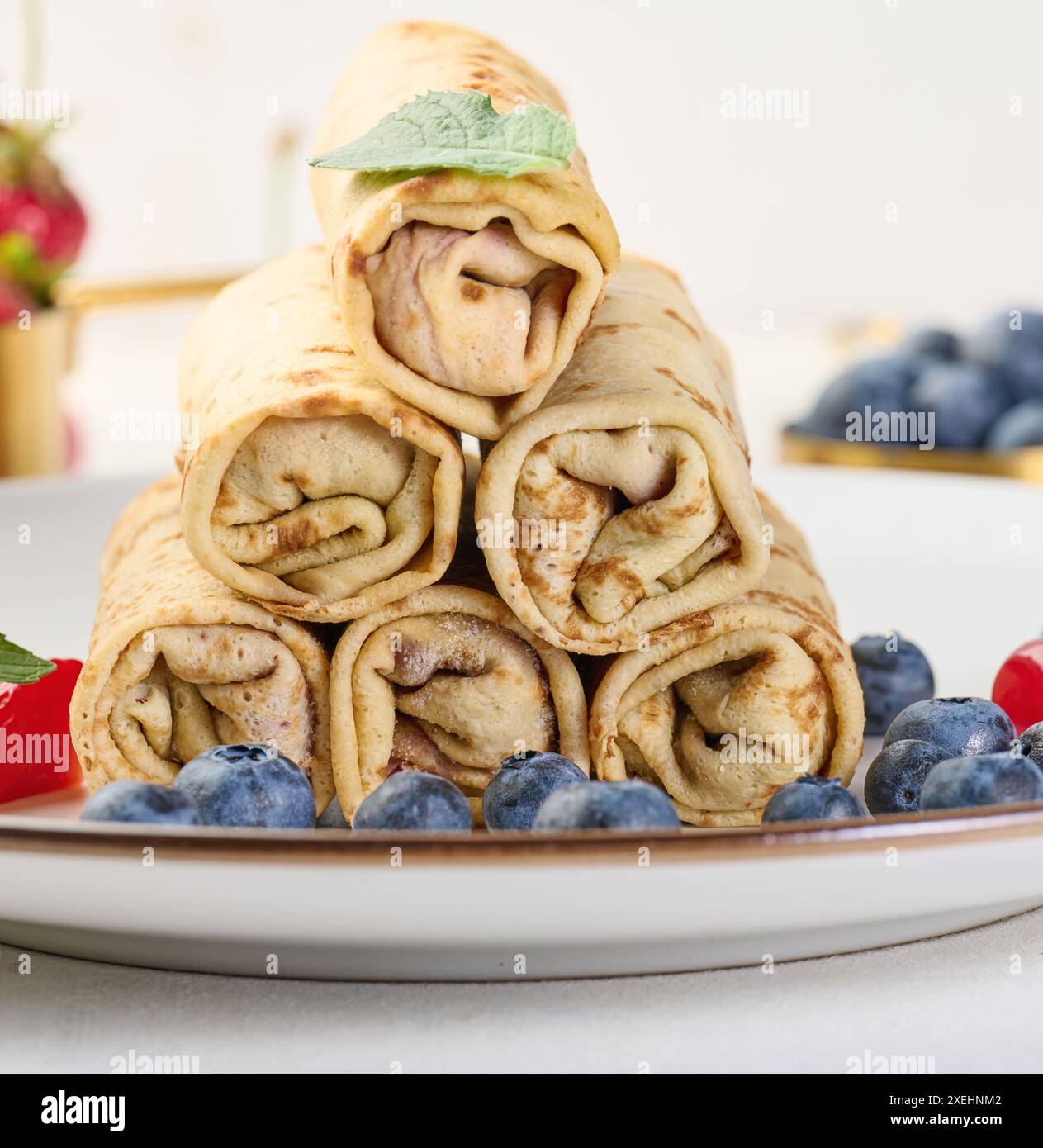 Stapel frittierte Crepes mit Füllung auf einem runden Teller, weißer Tisch Stockfoto