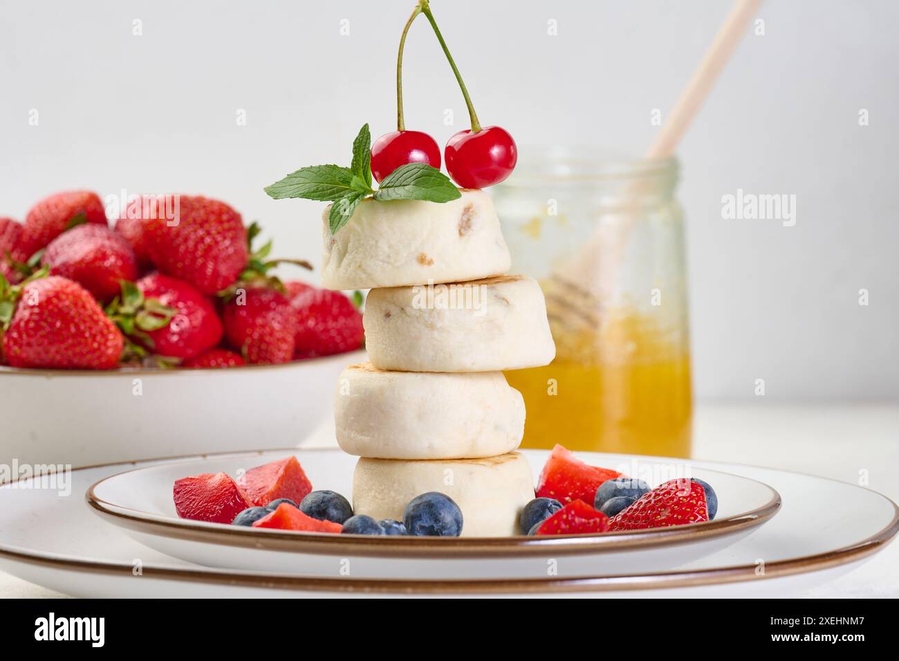 Ein Stapel von vier Käsekuchen auf einem Teller mit Beeren, Heidelbeeren, Erdbeeren und Kirschen. Stockfoto
