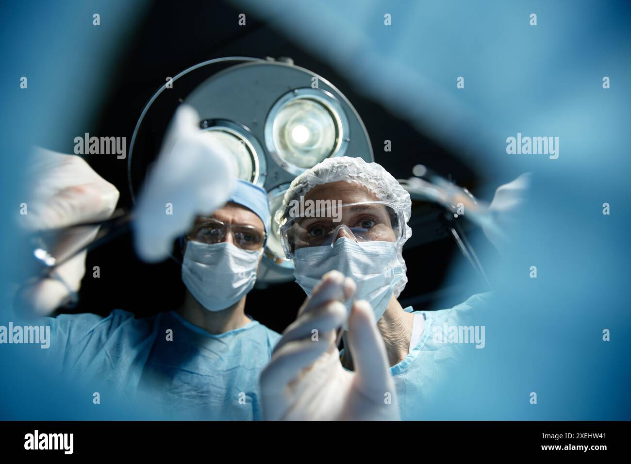 Tiefwinkelansicht zweier Chirurgen, die beim Tragen von Masken unter Operationslampen operieren und Werkzeuge halten Stockfoto