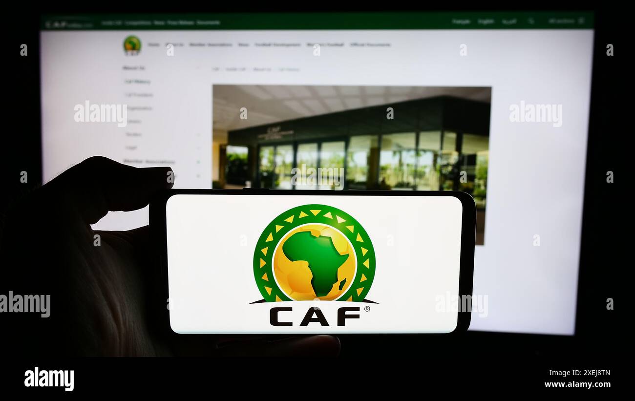 Person mit Handy mit Logo des Vereins Confederation Africaine de Football (CAF) vor der Webseite. Schwerpunkt auf dem Display des Telefons. Stockfoto