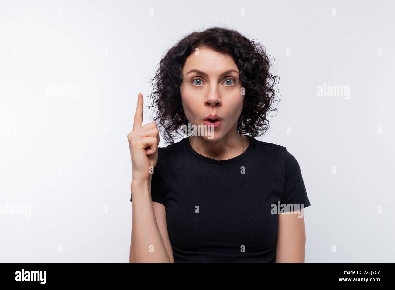 Erwachsene lockige europäische Frau, die ein schwarzes T-Shirt trägt, inspiriert von einer Idee Stockfoto