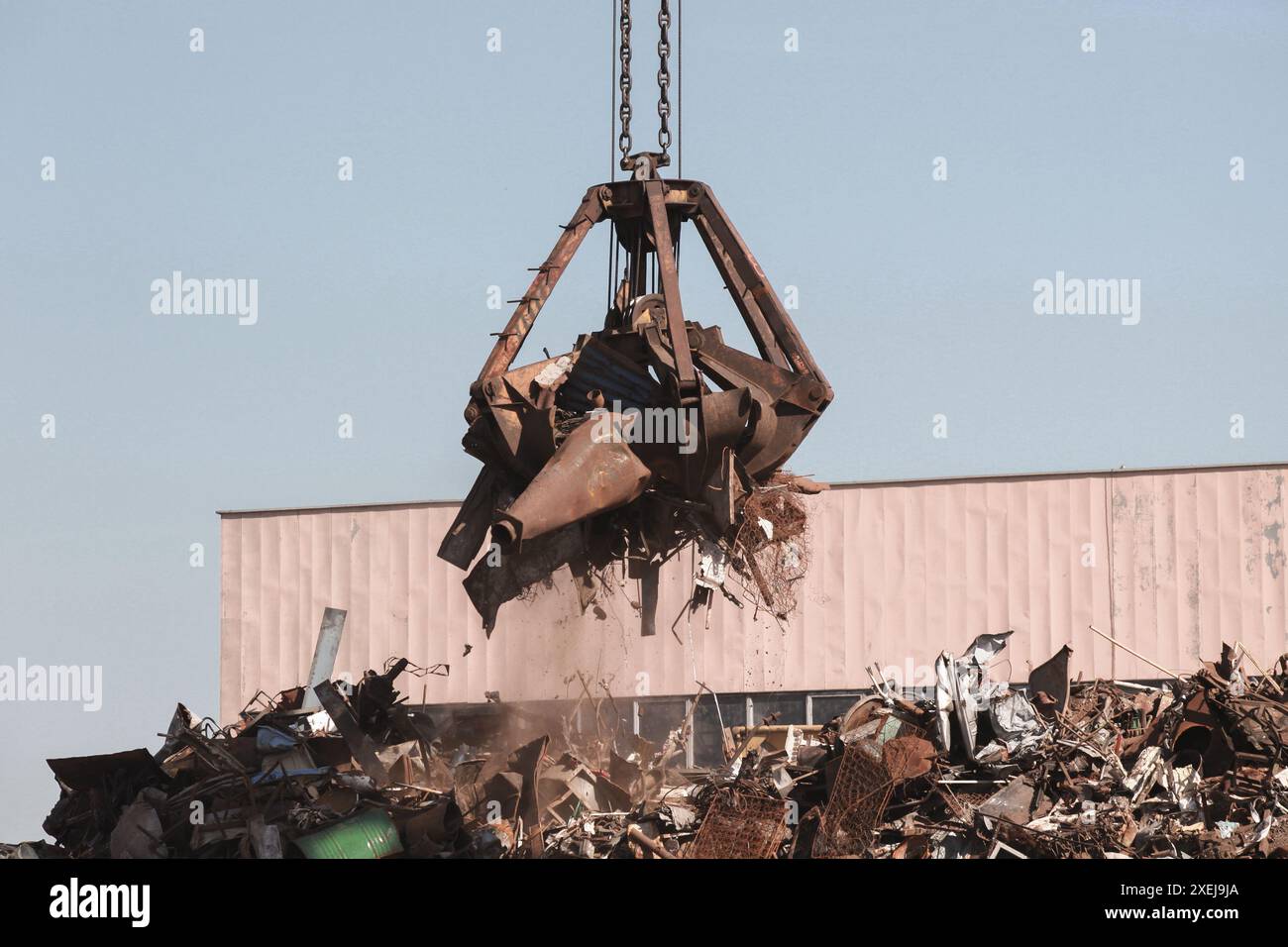 Hydraulischer Greifer transportiert rostiges Metallschrott zum Recycling an einem sonnigen Tag Stockfoto