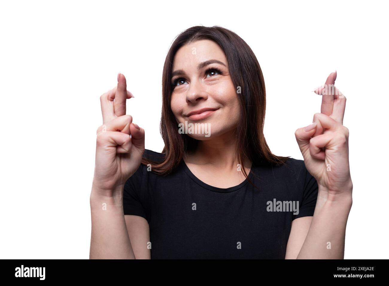 Eine junge, schöne Frau mit braunen Augen, die in einem schwarzen T-Shirt gekleidet ist, kreuzt ihre Finger Stockfoto