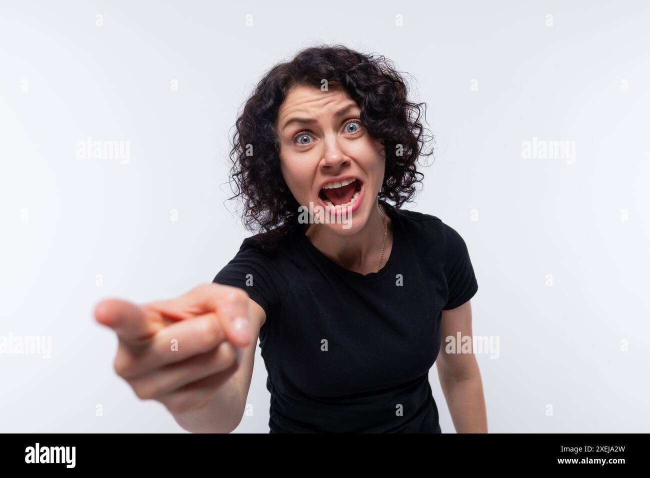 Eine wütende Brünette mit lockigen Haaren in einem schwarzen T-Shirt ist empört und schreit Stockfoto