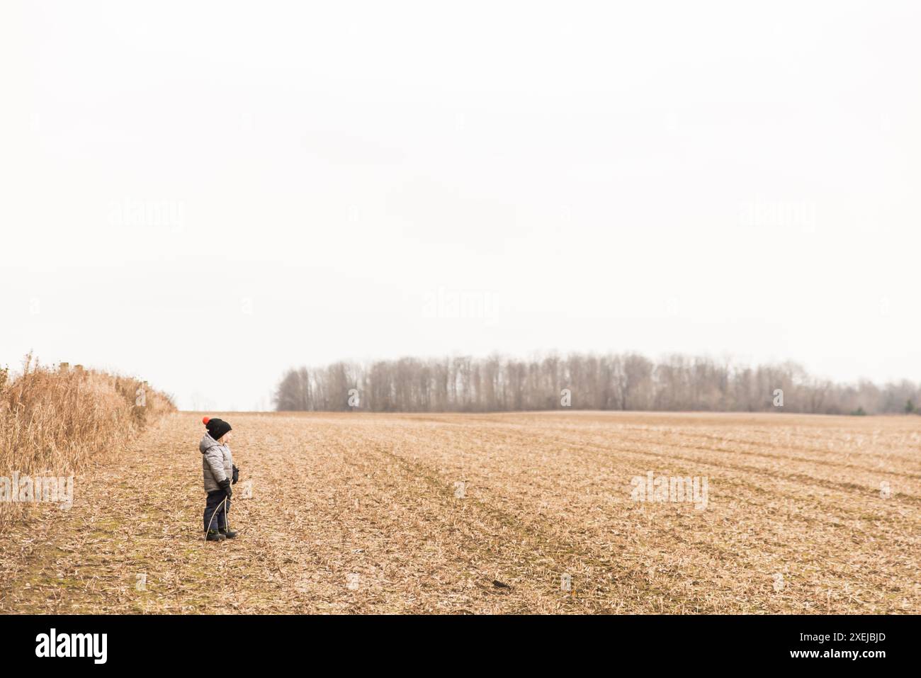 Kind, das im Winter auf einem kargen Feld steht und Winterkleidung trägt Stockfoto