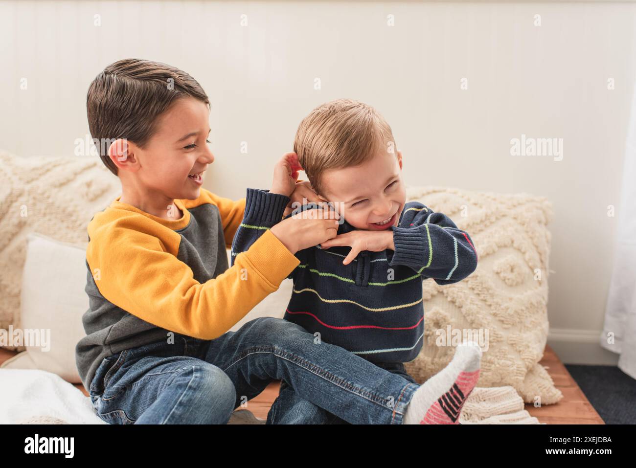 Fröhliche Brüder spielen zusammen und kitzeln, während sie zu Hause sitzen Stockfoto