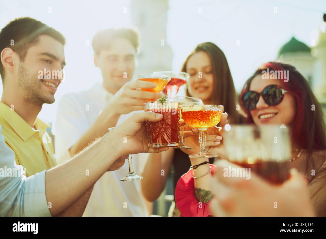 Lächelnde junge Erwachsene, Studenten genießen sonnige Treffen im Freien, knackende Gläser gefüllt mit bunten Getränken. Stockfoto