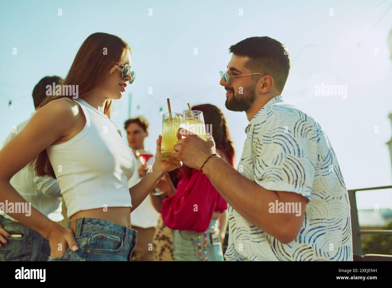 Freunde, Mann und Frau zwitschern ihre Gläser in festlichem Toast, ihre Gesichter leuchten mit Lächeln und Sonnenschein auf der Abendparty. Stockfoto