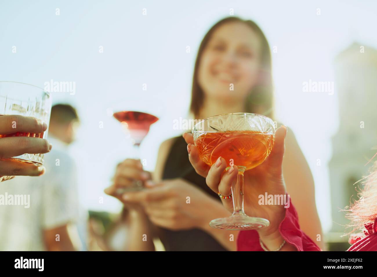Foto einer fröhlichen Gruppe von Freunden, Frauen und Männern, genießt den sonnigen Nachmittag und holt ihre Getränke in temperamentvollem Toast. Stockfoto