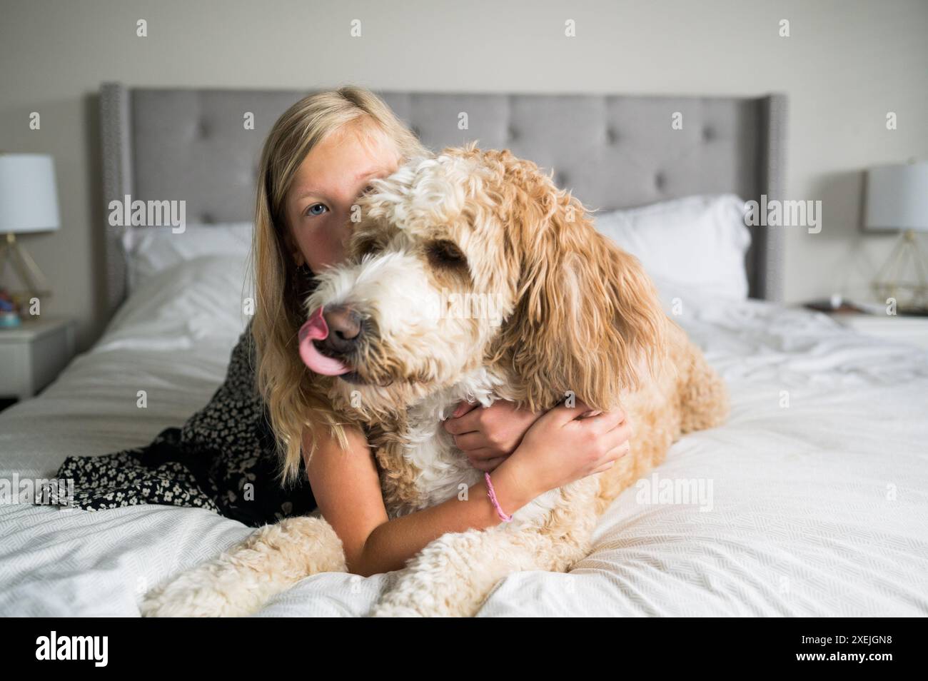 Ein junges Mädchen und ein flauschiger Hund lagen auf einem Bett Stockfoto