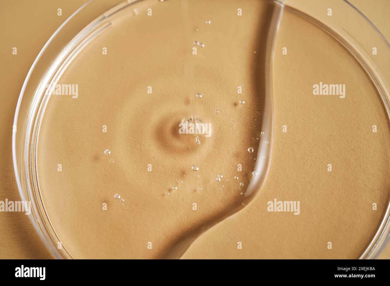 Serum oder Kosmetiköl fließt in eine transparente Schüssel. Stockfoto