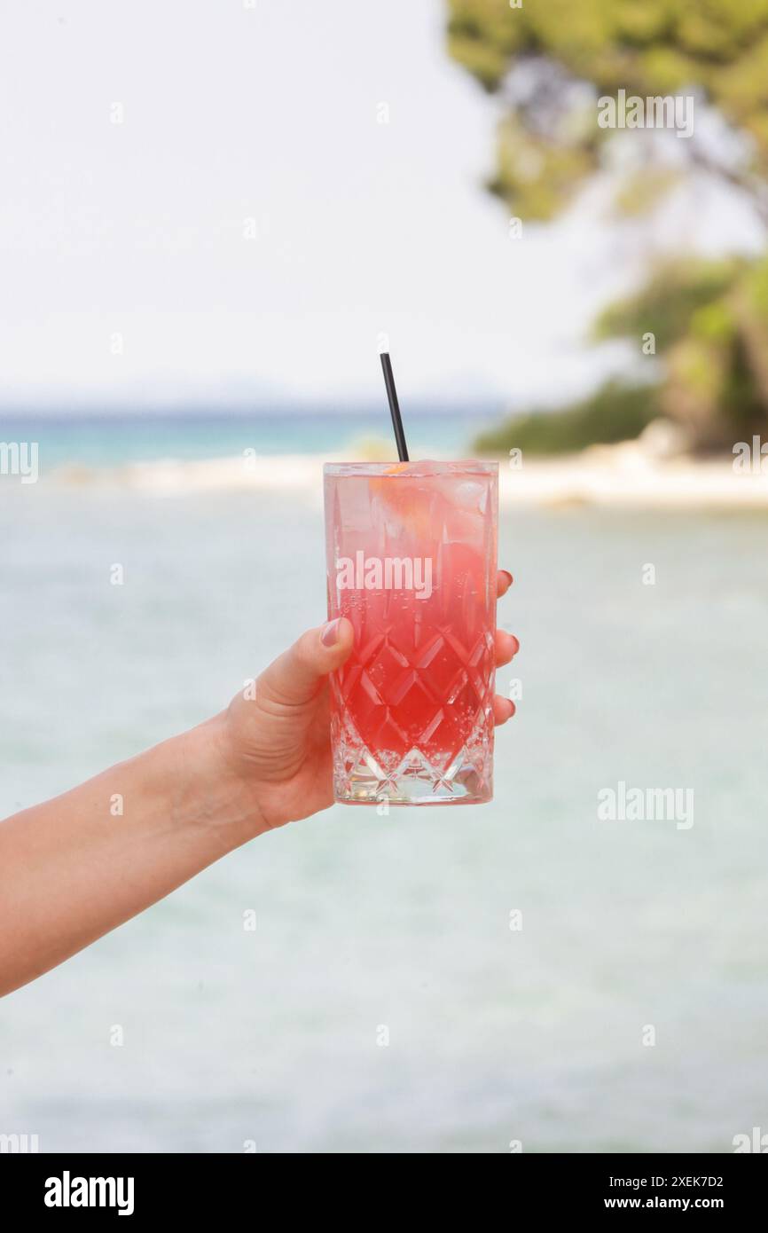 Frau hält ein Glas mit einem roten erfrischenden Getränk vor der blauen See, Cold-Brew-Iced-Sweet-Hibiscus-Tee, sommerliches Erfrischungsgetränk, Detox, Diät und Gesundheit Stockfoto