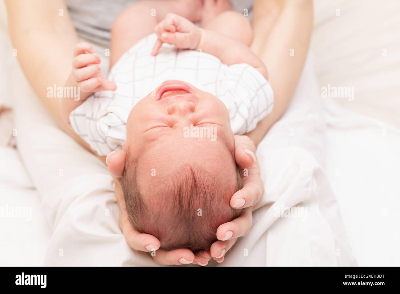 Die Mutter wiegt ihr weinendes Neugeborenes in ihren Armen und hält sanft den Kopf des Babys Stockfoto