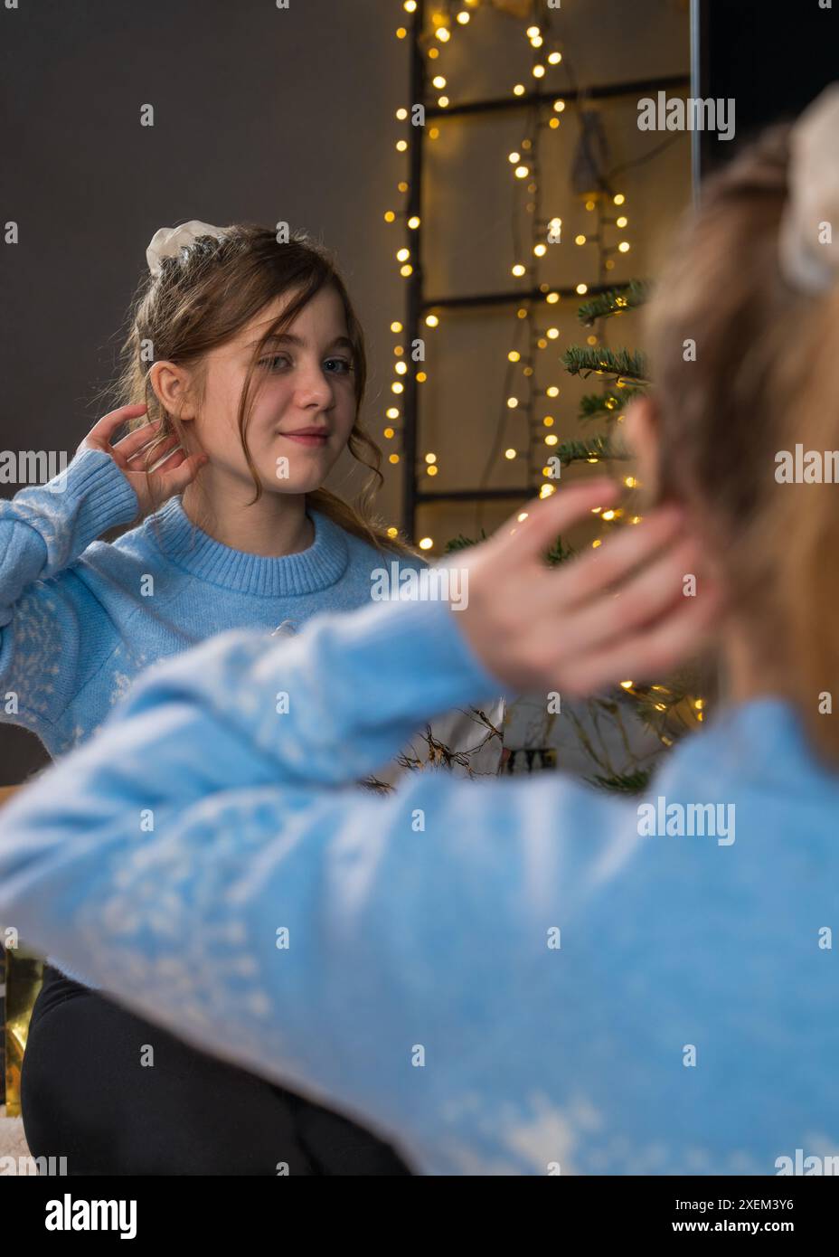 Porträt eines 13-jährigen Mädchens. Das Mädchen bewundert ihr Spiegelbild im Spiegel. Vor dem Hintergrund einer glühenden Girlande und Lichtern. Stockfoto