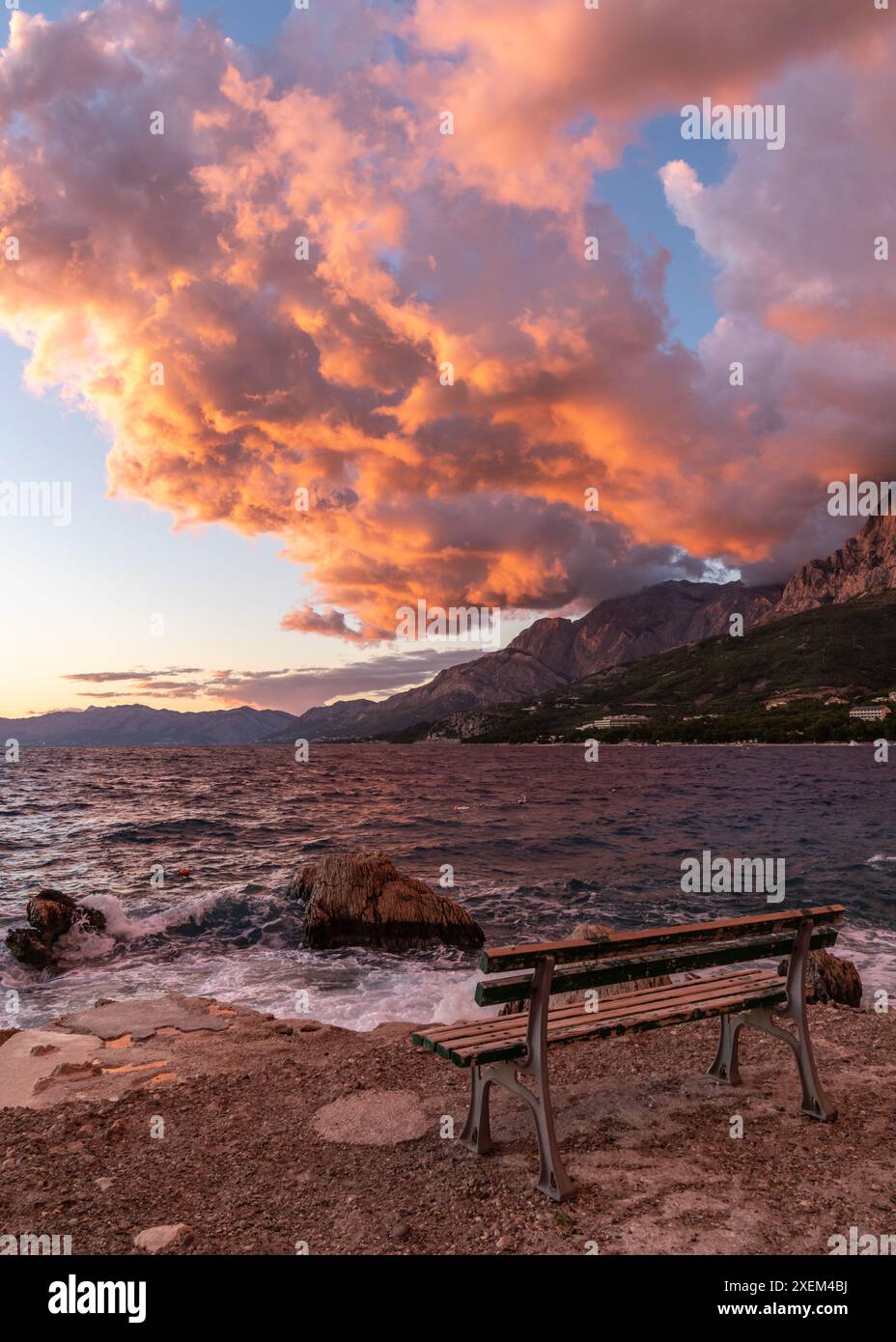 Wunderschöner Sonnenuntergang auf dem Meer. Die untergehende Sonne malte die Berglandschaft, das Meer in rot-oranger Farbe. Es gibt eine einsame Holzbank am Strand. Stockfoto