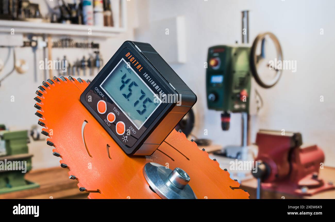 Elektronischer Neigungsmesser mit digitaler Anzeige auf orangefarbener Scheibe der elektrischen Gehrungssäge. Nahaufnahme des präzisen Werkzeugs zur Messung der Steigung angle.inside im Arbeitsraum. Stockfoto