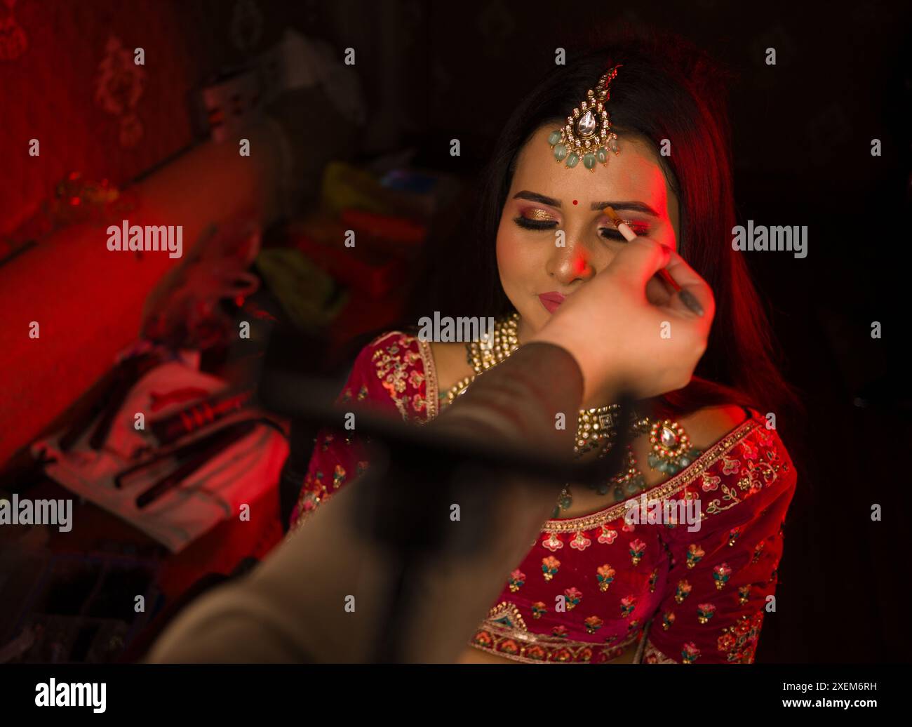 Eine Nahaufnahme der Hand eines Make-up-Künstlers, der eine indische Braut in traditioneller Kleidung zubereitet, verziert mit kompliziertem Schmuck Stockfoto