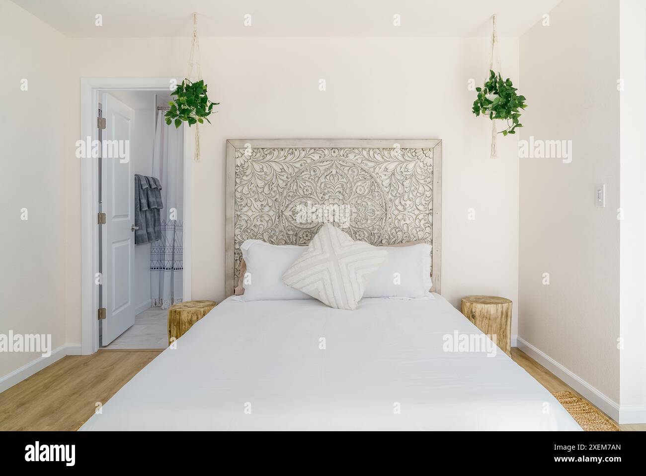 Modernes Schlafzimmer mit Boho-Bett und geschnitztem Kopfteil aus Holz und Baumstumpf-Beistelltische mit hängenden Pflanzen Stockfoto