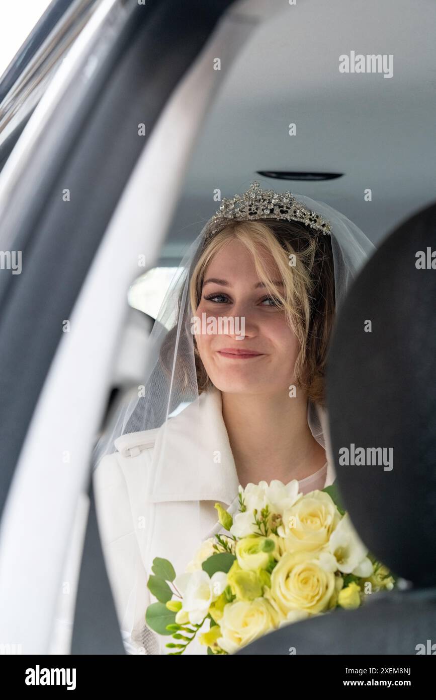 Eine schöne, junge Braut mit einem großen Strauß weißer Rosen sitzt in einem Auto und wartet auf den Bräutigam. Warten, Hochzeit Stockfoto